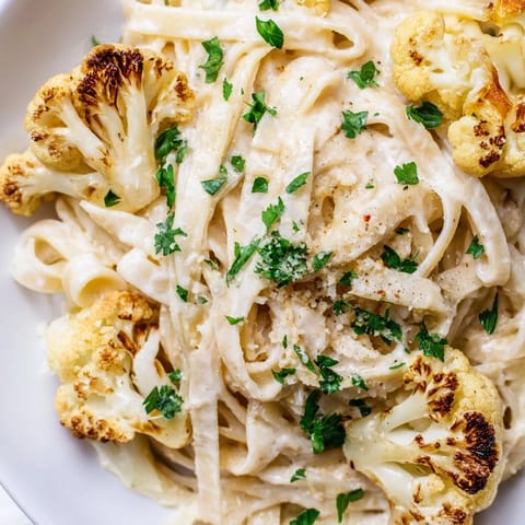 Roasted Cauliflower Alfredo pasta twirled on a fork, showcasing a silky, nutmeg-infused sauce made from blended cauliflower and garlic.