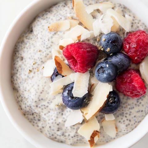 A close-up of creamy Poppy Seed Chia Pudding in a glass jar, topped with fresh blueberries and toasted almonds.  