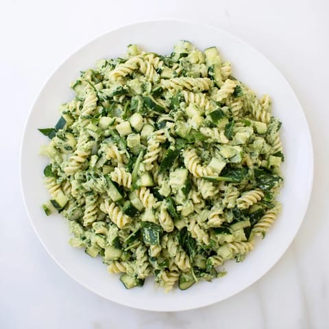 A close-up of vibrant Green Goddess Pasta Salad with fusilli, diced cucumbers, and fresh herbs in a creamy avocado-yogurt dressing.