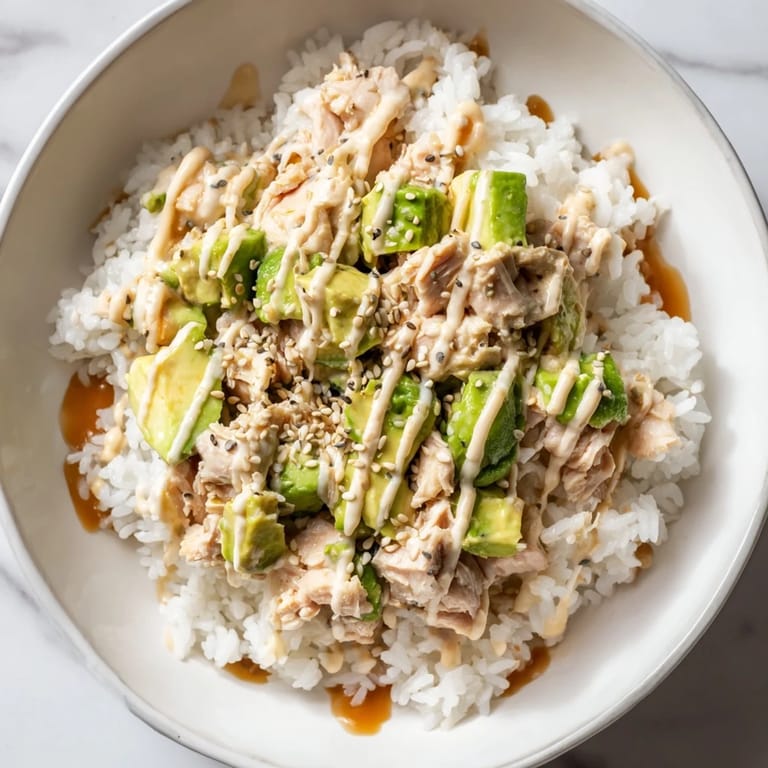 A vibrant Tuna Avocado Rice Bowl features a drizzle of savory soy-ginger dressing and toasted sesame seeds over fresh, colorful ingredients.  