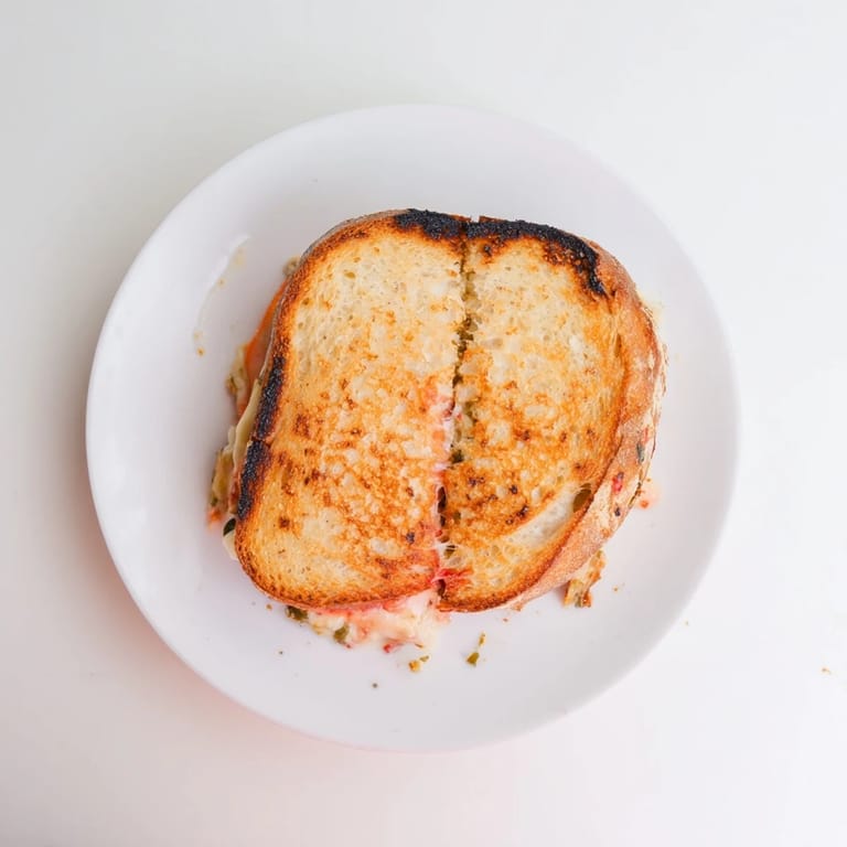 A close-up of Pepper Jack & Tomato Grilled Cheese on a cutting board, sliced to show layers.