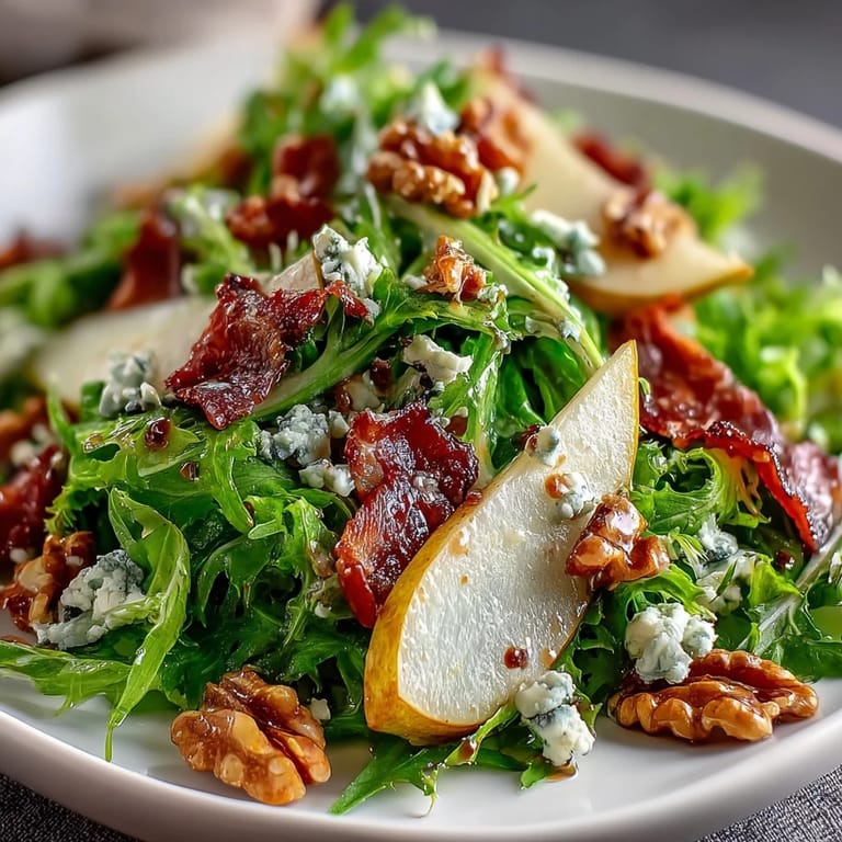 Juicy pear slices and creamy blue cheese top a fresh Frisée, Pear, Blue Cheese, and Crispy Prosciutto Salad in a rustic bowl.