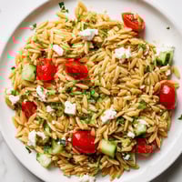 A close-up of Greek Orzo Salad, with orzo, tomatoes, cucumber, and feta cheese drenched in zesty lemon-oregano dressing.