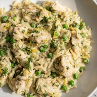 Savory lemon herb chicken orzo skillet simmering with tender pieces, bright green peas, and fresh parsley in a zesty sauce.  
