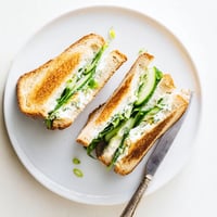 Golden-brown Whipped Feta Spring Grilled Cheese oozing with creamy dill filling, served beside fresh lemon slices.